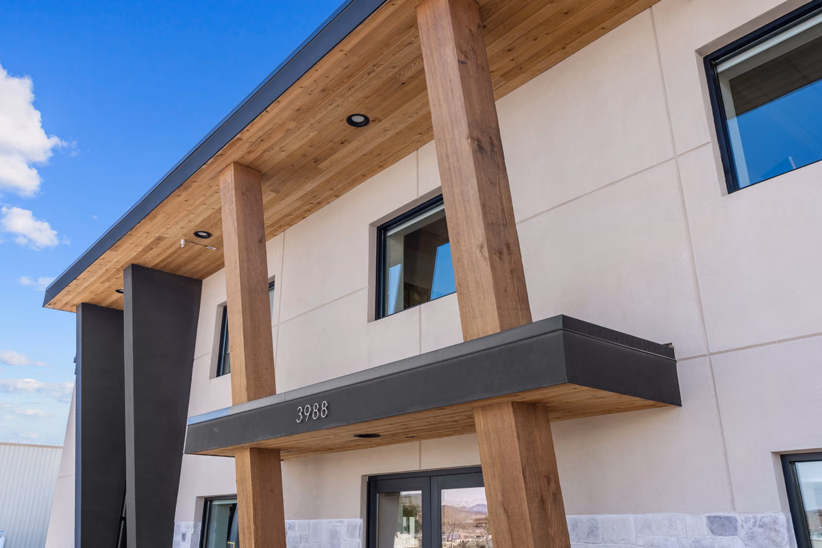 Upward view of the entry canopy with a cedar soffit and recessed lights, square cedar posts, a black fascia showing the address 3988, and stone veneer at the base.
