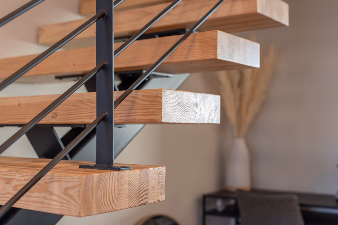 Close view of timber stair treads on a black steel post and rod railing, with a dried pampas arrangement in a vase in the background.