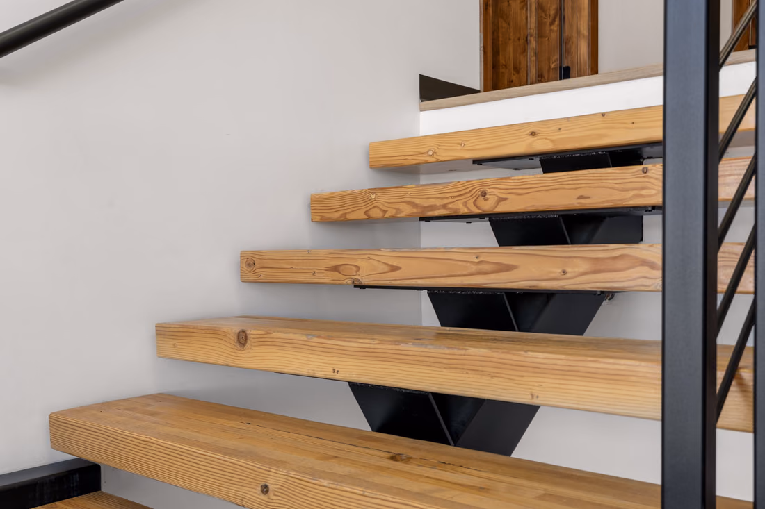 Close view of solid timber stair treads on black steel brackets beside a black steel post, with a wooden door at the top of the stair.